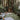Bohemian-style outdoor lounge with woven rattan sofa, patterned rugs, and cozy cushions, set in a lush forest retreat with a wooden treehouse.